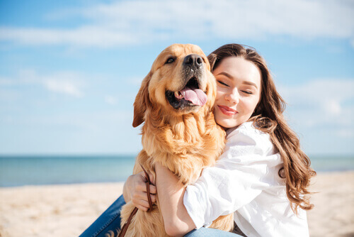 Dona abraçando cachorro na praia