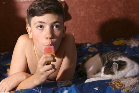 Menino chupando picolé ao lado de gatinho